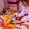 BIBS Glass Baby Bottle in Baby Blue, 120 ml, with a slow flow nipple, held by a toddler on a colorful striped cushion.