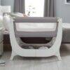 Shnuggle Air Bedside Crib in Dove Grey with a mesh side panel, positioned beside a bed in a cozy nursery setting.