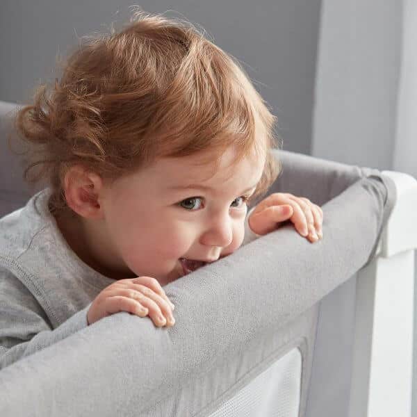 Shnuggle Air Cot Conversion Kit in Dove Grey, featuring a child playfully leaning over the edge of the cot.