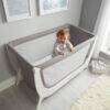 Shnuggle Air Cot Conversion Kit in Dove Grey with a smiling baby standing inside, set in a bright nursery.