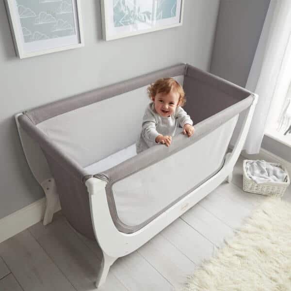 Shnuggle Air Cot Conversion Kit in Dove Grey with a smiling baby standing inside, set in a bright nursery.