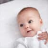 Shnuggle 100% Cotton 3-pack Air Crib Bedding Set with a smiling baby lying on a soft, patterned crib sheet.
