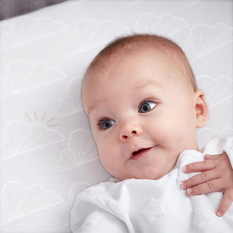 Shnuggle 100% Cotton 3-pack Air Crib Bedding Set with a smiling baby lying on a soft, patterned crib sheet.