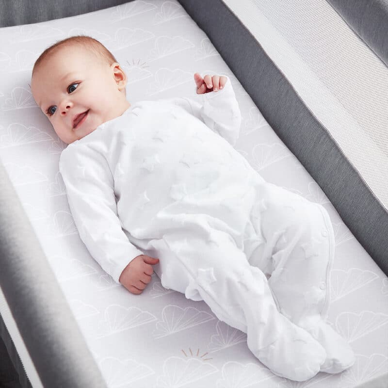 Shnuggle 100% Cotton 3-pack Air Crib Bedding Set with a smiling baby in a white outfit lying on a crib mattress.