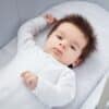 Shnuggle Dreami Moses Basket fitted sheets in grey, featuring a soft design, with a baby lying comfortably on one.