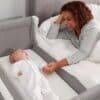 Shnuggle Air Bedside Crib in Dove Grey, featuring a parent interacting with a baby, cozy nursery setting.