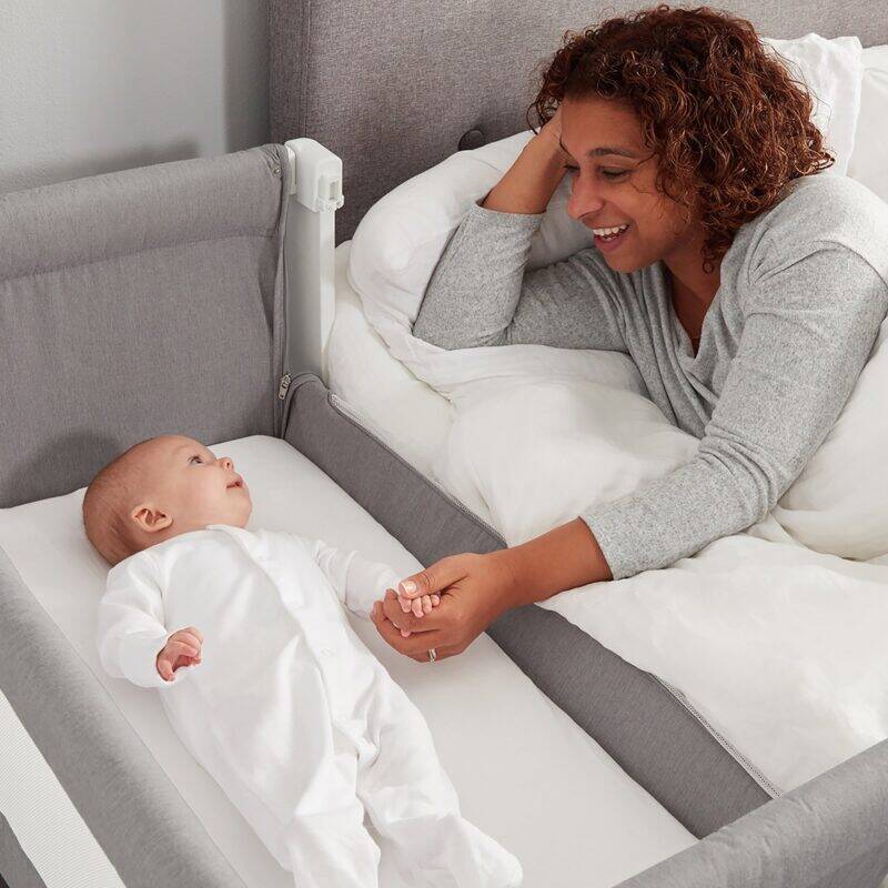Shnuggle Air Bedside Crib in Dove Grey, featuring a parent interacting with a baby, cozy nursery setting.