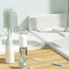 Momcozy Bottle Brush Kit in mint green with a large brush, cleaning solution, and small brush on a wooden countertop.