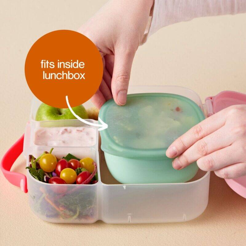 b.box lunch tub in berry smoothie with green container, showcasing a hand placing it inside a lunchbox with healthy snacks.