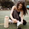 b.box 1L insulated water bottle in berry smoothie, placed beside a girl tying her shoelaces on a sports court.