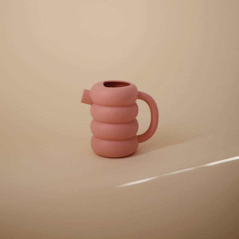 Mushie Silicone Watering Can in Peony, featuring a unique ribbed design and ergonomic handle, set against a soft background.