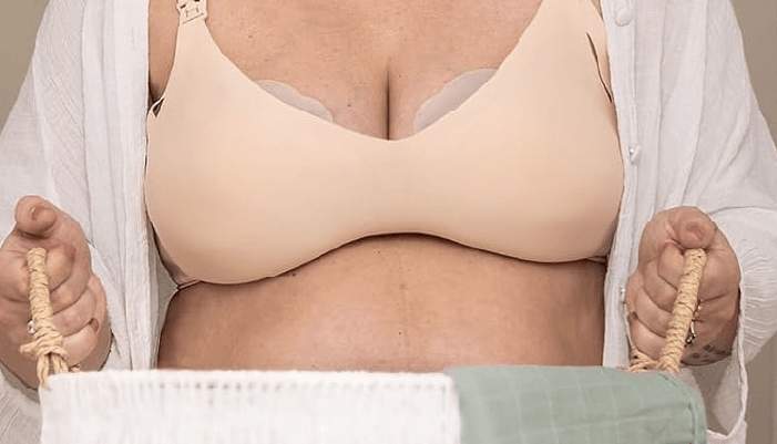 Haakaa Petal Soft Milk Collector in use, held by a person wearing a nude bra, showcasing its discreet design.