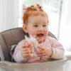 Back to Nature Wood Ring Rattle in pink, held by a smiling baby in a high chair, showcasing a playful moment.