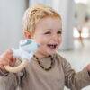 Back to Nature Wood Ring Rattle in blue and pink, held by a smiling toddler, showcasing a playful and engaging design.
