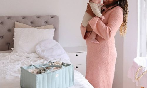 Mushie Diaper Caddy in Blue Flowers and Blush, placed on a bed, with a mother holding her baby nearby.