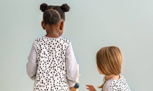 Love To Dream Sleep Suit Long Sleeve 1.0 Tog in white with animal print, featuring two children playing with a wooden toy.