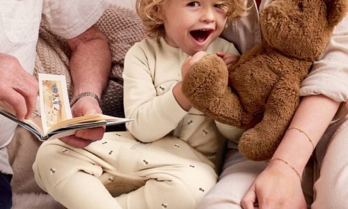 Love to Dream Sleep Suit Long Sleeve 2.5 TOG in Oatmeal Bees, child smiling while holding a teddy bear with family.