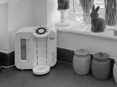 White countertop water dispenser with a circular control panel, placed next to decorative jars and rabbit figurines.